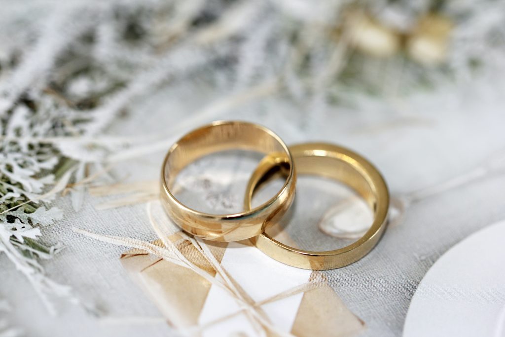 Gold wedding rings resting on a table beside a white plate, symbolizing love and commitment.
