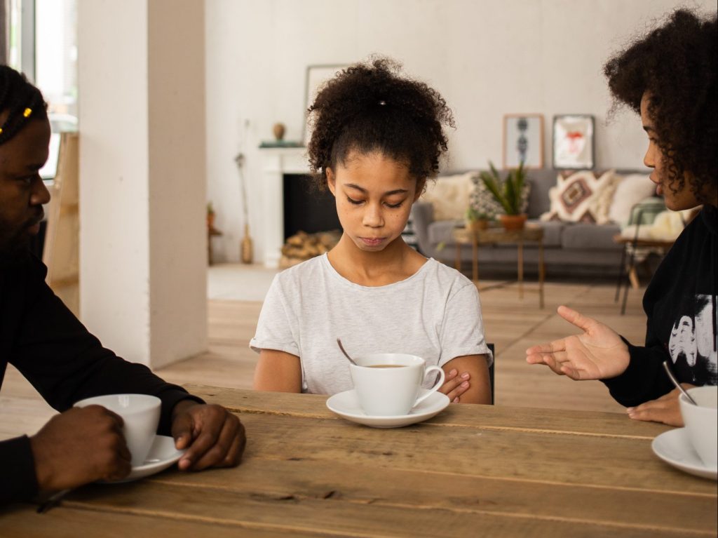 Child Sitting at table being chastised by 2 adults