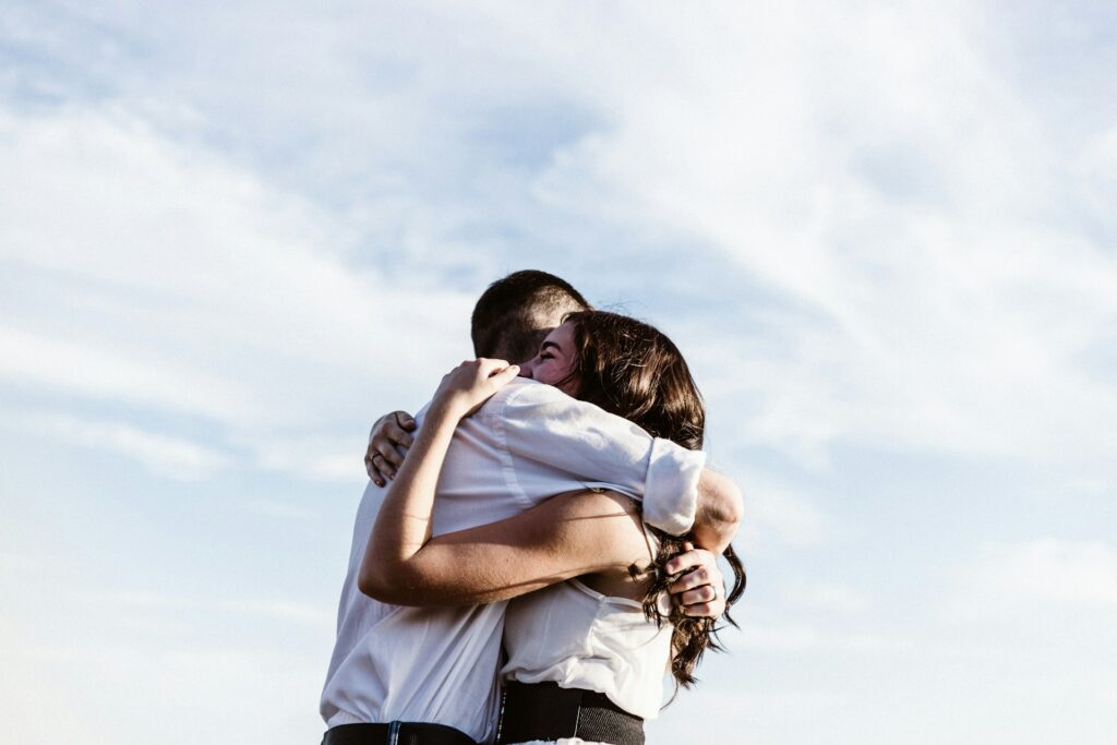 A man and woman are seen embracing, framed by a vibrant blue sky, representing their bond and affection for one another.
