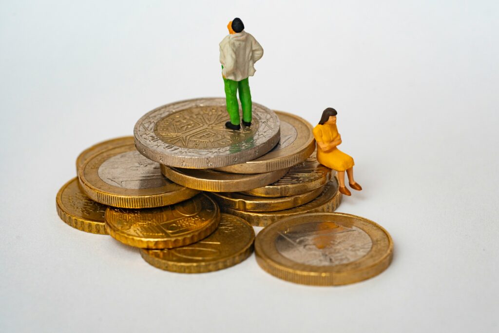 Miniature couple standing on a pile of coins, symbolizing a disagreement over financial matters.