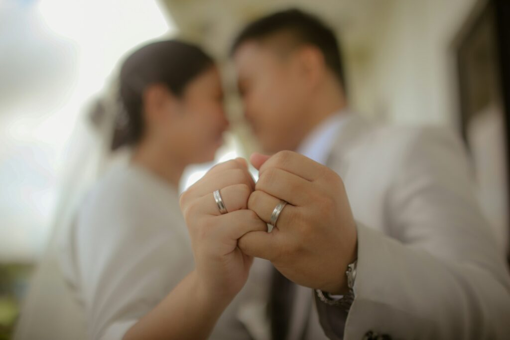A bride and groom join hands, highlighting their wedding rings in the foreground, signifying unity.