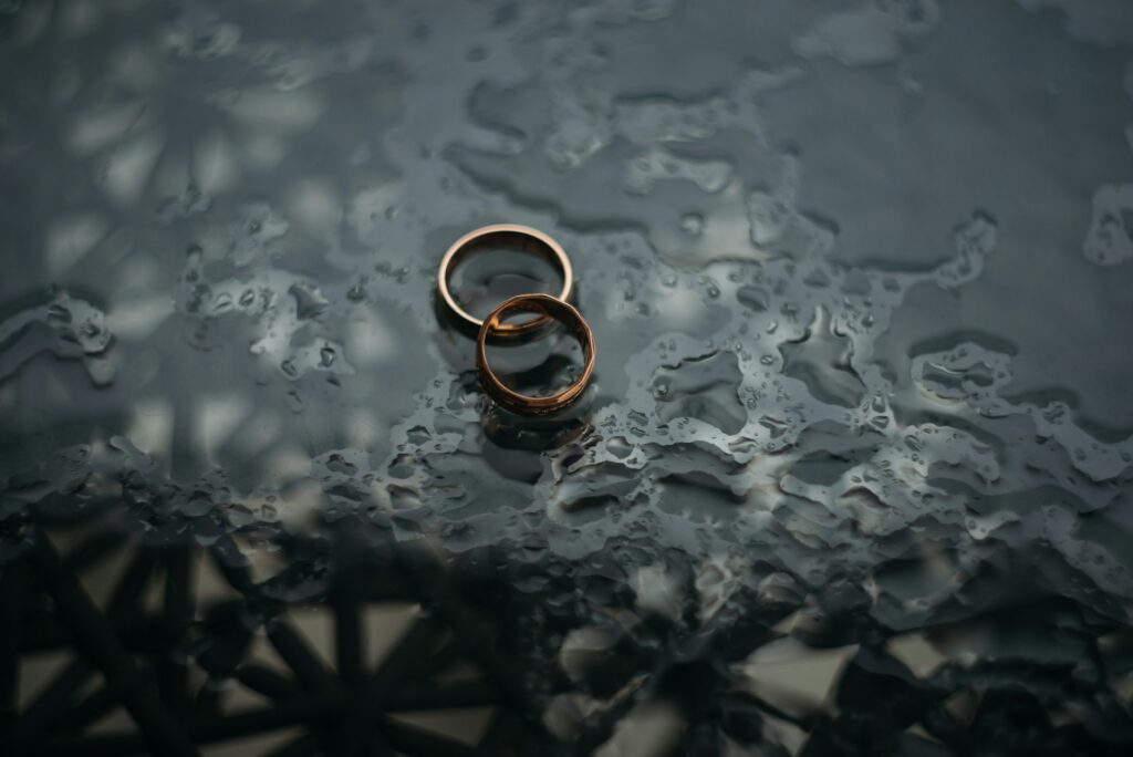 Two wedding rings resting on a table, glistening with water droplets from the rain.